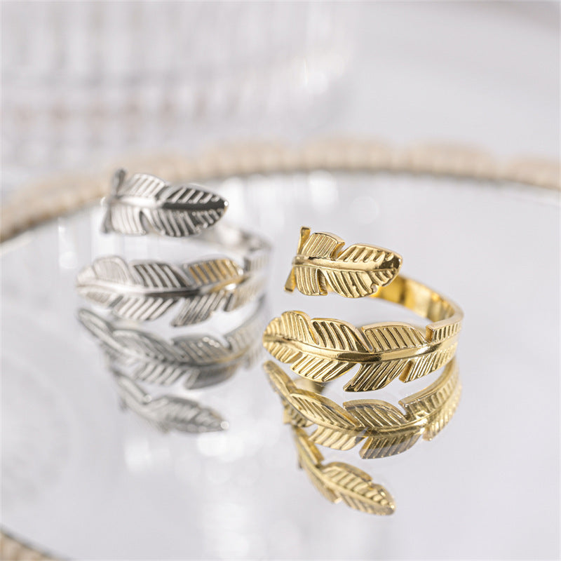 Gold and silver feather-shaped rings on a reflective surface