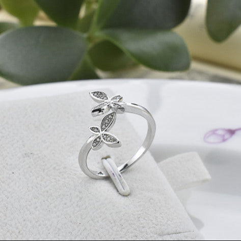 Silver open ring with leaf design on a white surface with green leaves in the background