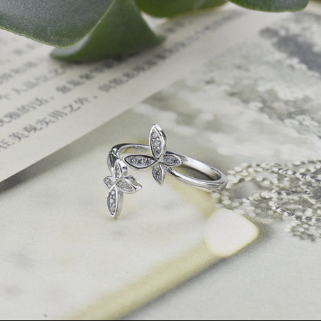 Silver butterfly ring on a marble surface with a plant and paper in the background