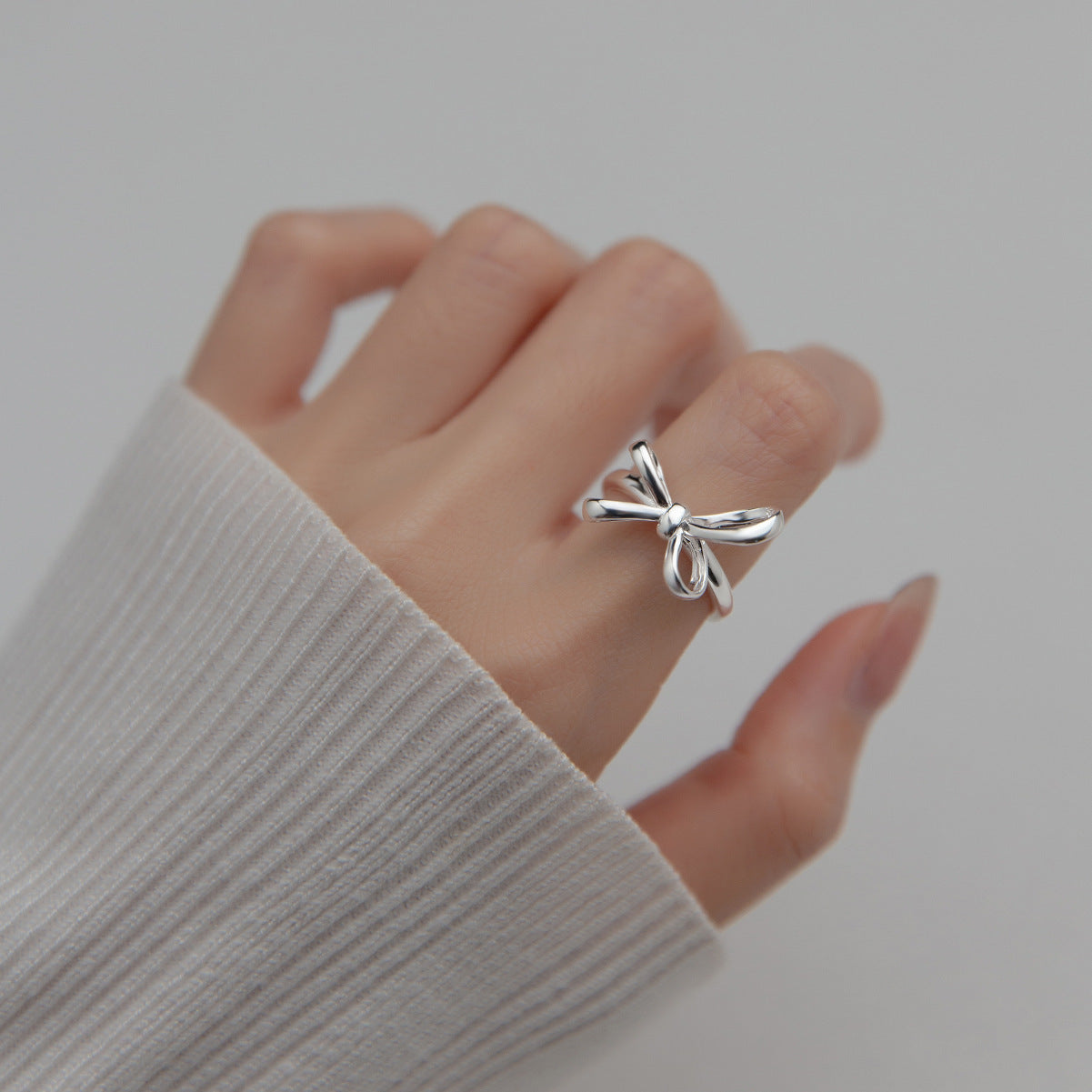 Silver bow-shaped ring on a finger with a neutral background