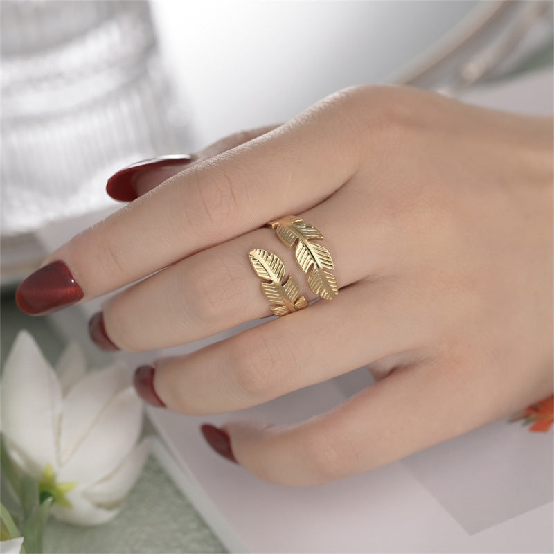 Gold feather ring on a hand with red nail polish, blurred background