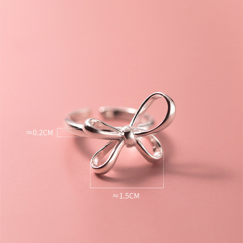 Silver bow-shaped ring on a pink background with measurements indicated.
